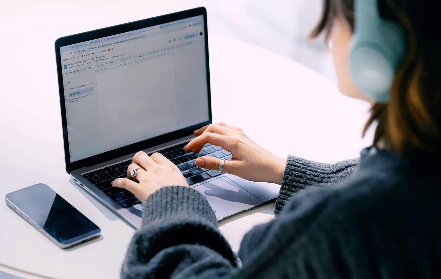 A person working on a laptop with a smartphone on a white table, representing AI content generation and technology workflow at Texlabai.